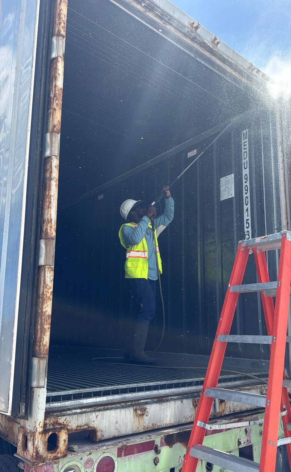 Technician pressure-washing the interior of a container from a ladder